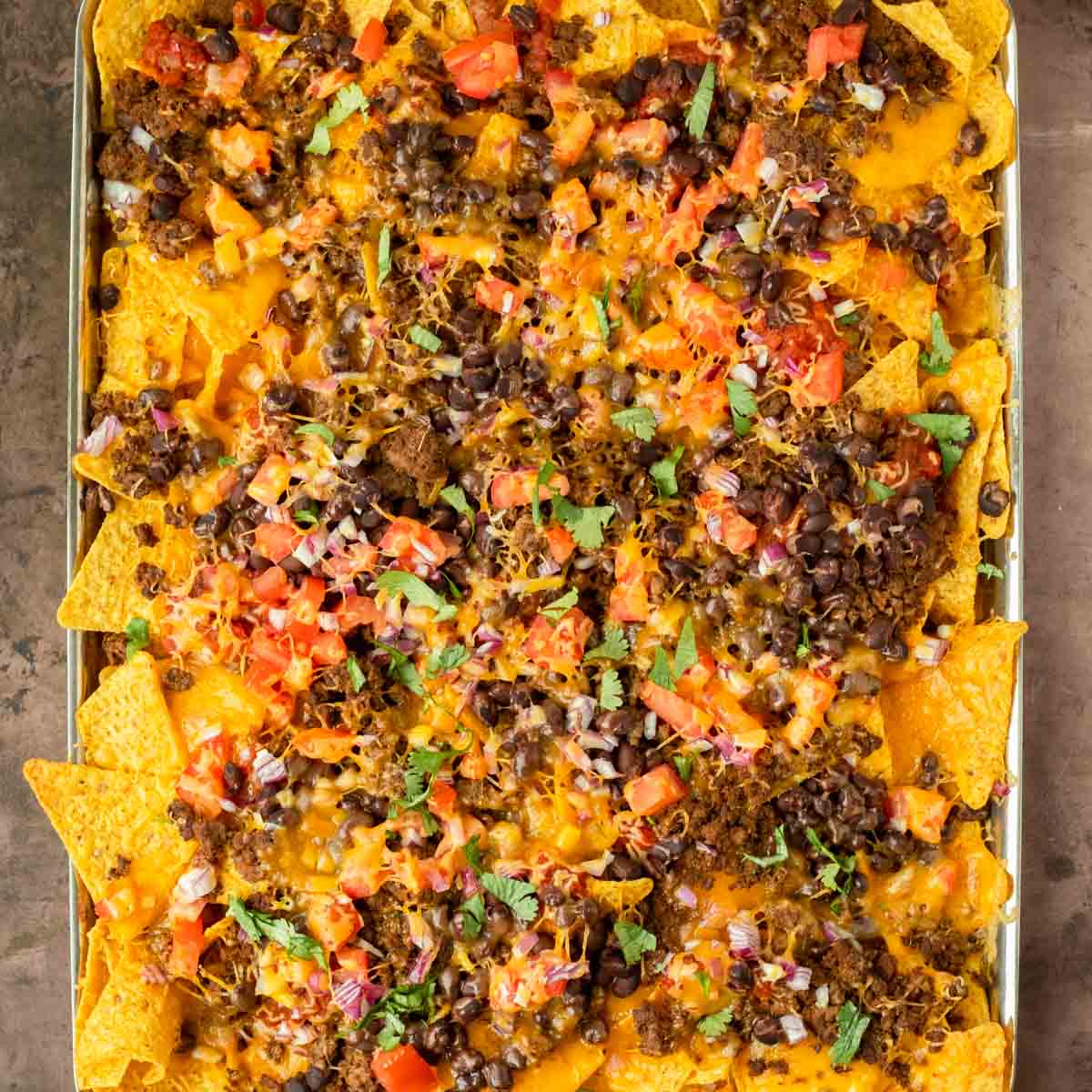 These sheet pan nachos are an easy appetizer recipe made with pantry-staple ingredients for a quick and flavorful crowd-pleaser dish. This recipe can be served for a game day appetizer but is also a great quick weeknight meal.