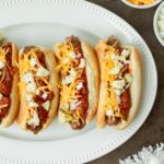 These loaded chili brats are a classic summer cookout recipe and easy weeknight dinner made with grilled brats topped with homemade chili and classic toppings.