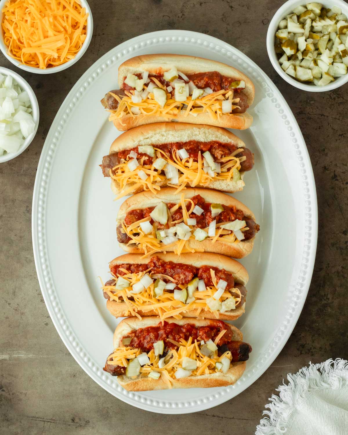 These loaded chili brats are a classic summer cookout recipe and easy weeknight dinner made with grilled brats topped with homemade chili and classic toppings.