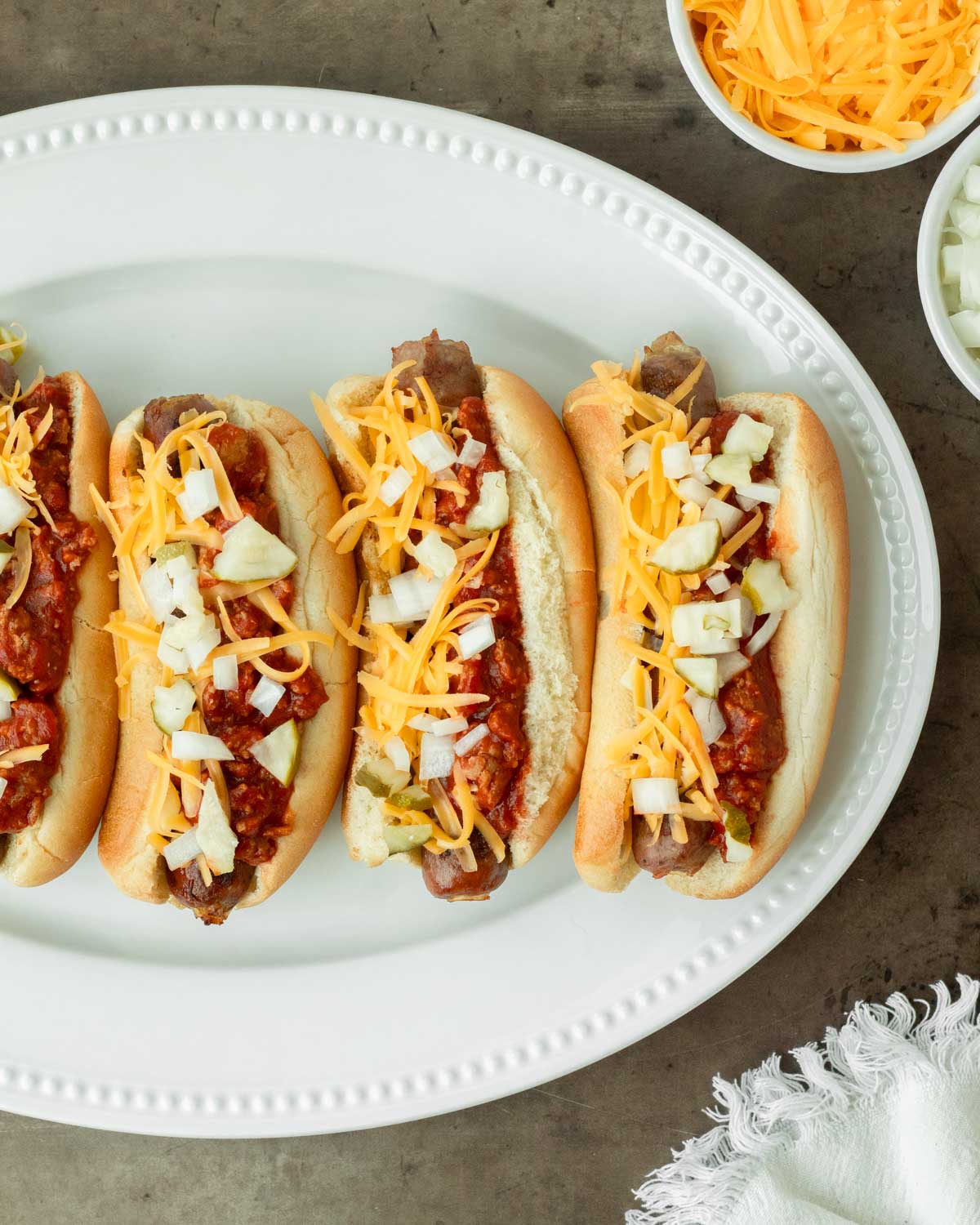 These loaded chili brats are a classic summer cookout recipe and easy weeknight dinner made with grilled brats topped with homemade chili and classic toppings.