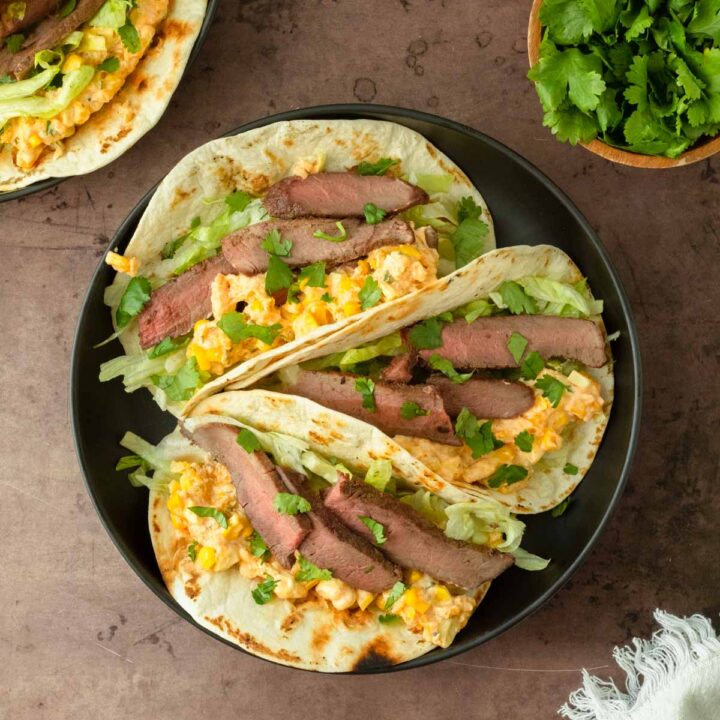 These street corn steak tacos are a delicious grilled steak taco topped with lettuce, cilantro, and homemade street corn dip for a flavorful and easy dinner recipe.