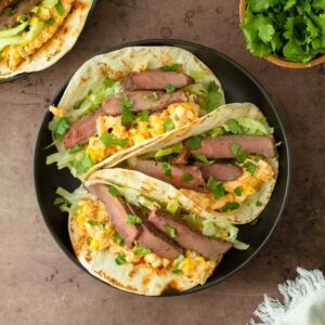 These street corn steak tacos are a delicious grilled steak taco topped with lettuce, cilantro, and homemade street corn dip for a flavorful and easy dinner recipe.