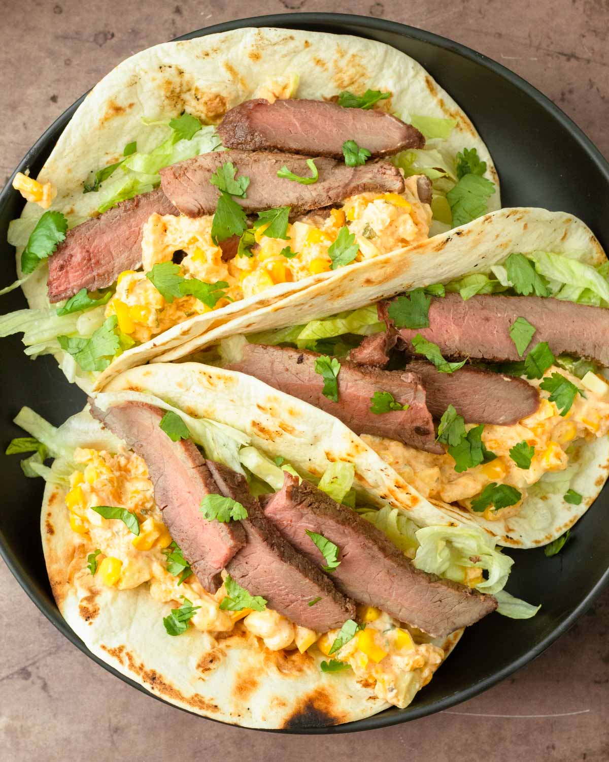 These street corn steak tacos are a delicious grilled steak taco topped with lettuce, cilantro, and homemade street corn dip for a flavorful and easy dinner recipe.