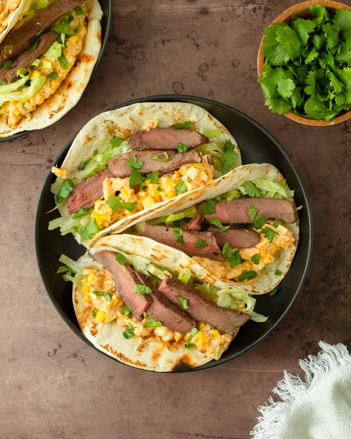 These street corn steak tacos are a delicious grilled steak taco topped with lettuce, cilantro, and homemade street corn dip for a flavorful and easy dinner recipe.